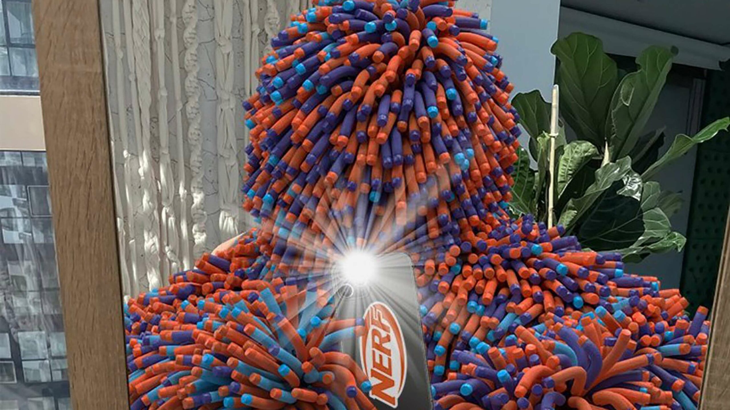 Nerf's new mascot Murf. They are standing in front of a mirror and taking a selfie using a phone with a case that says Nerf.